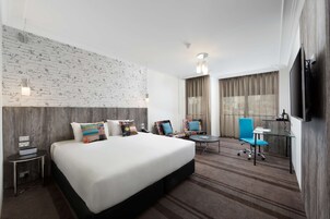 A hotel room with a large bed, a desk, two chairs, a TV, and a brick-patterned wall.