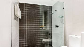 Un baño moderno con cabina de ducha de vidrio, inodoro blanco y suelo de baldosas.