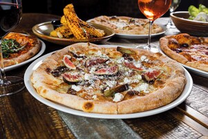 Ein Tisch mit mehreren Pizzen, einer Schüssel Maiskolben und einem Weinglas.