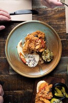 Un plato de pollo frito con salsa y una cuña de lima sobre una mesa de madera rústica.