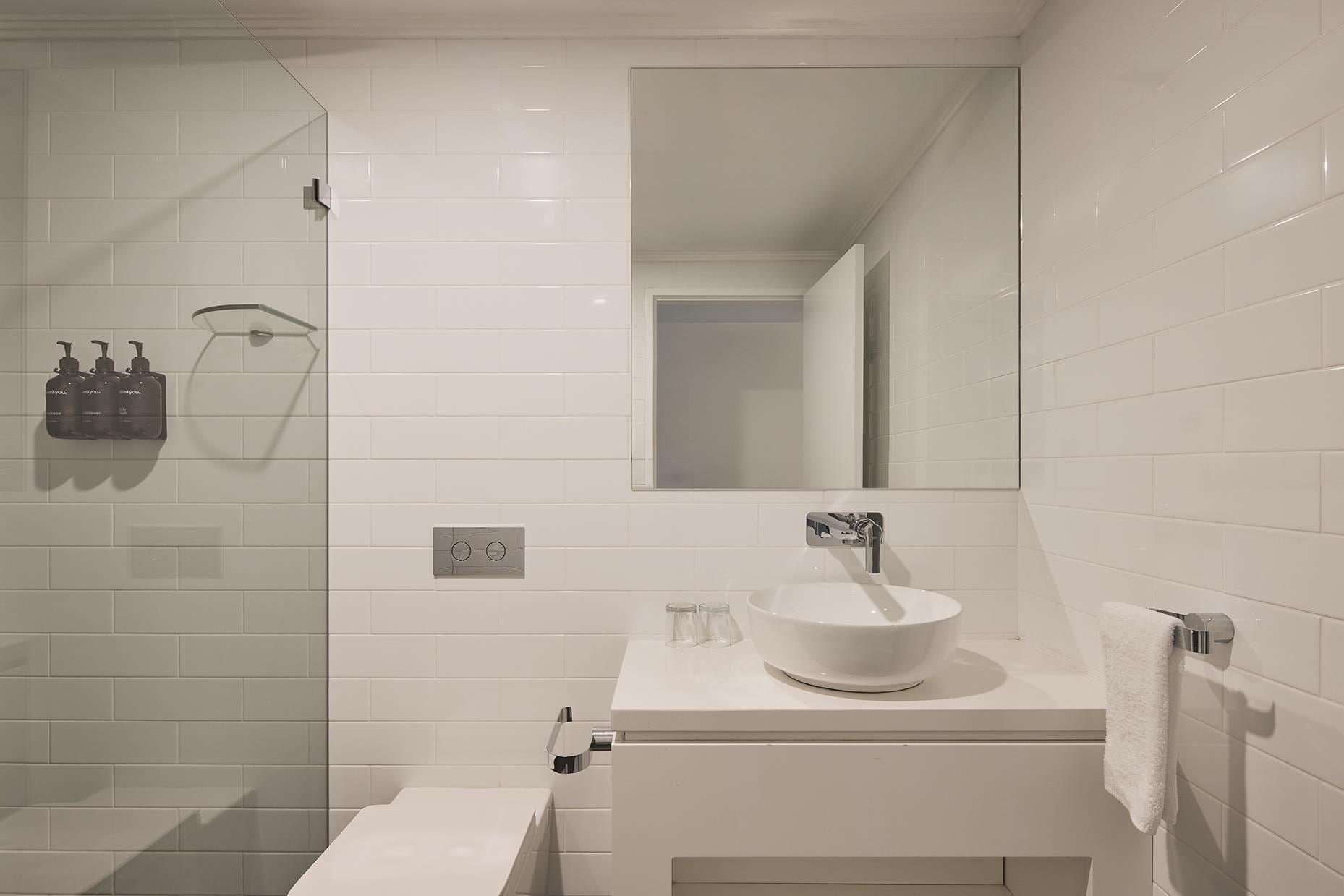 Un baño moderno con lavabo blanco, espejo y cabina de ducha con mampara de vidrio.