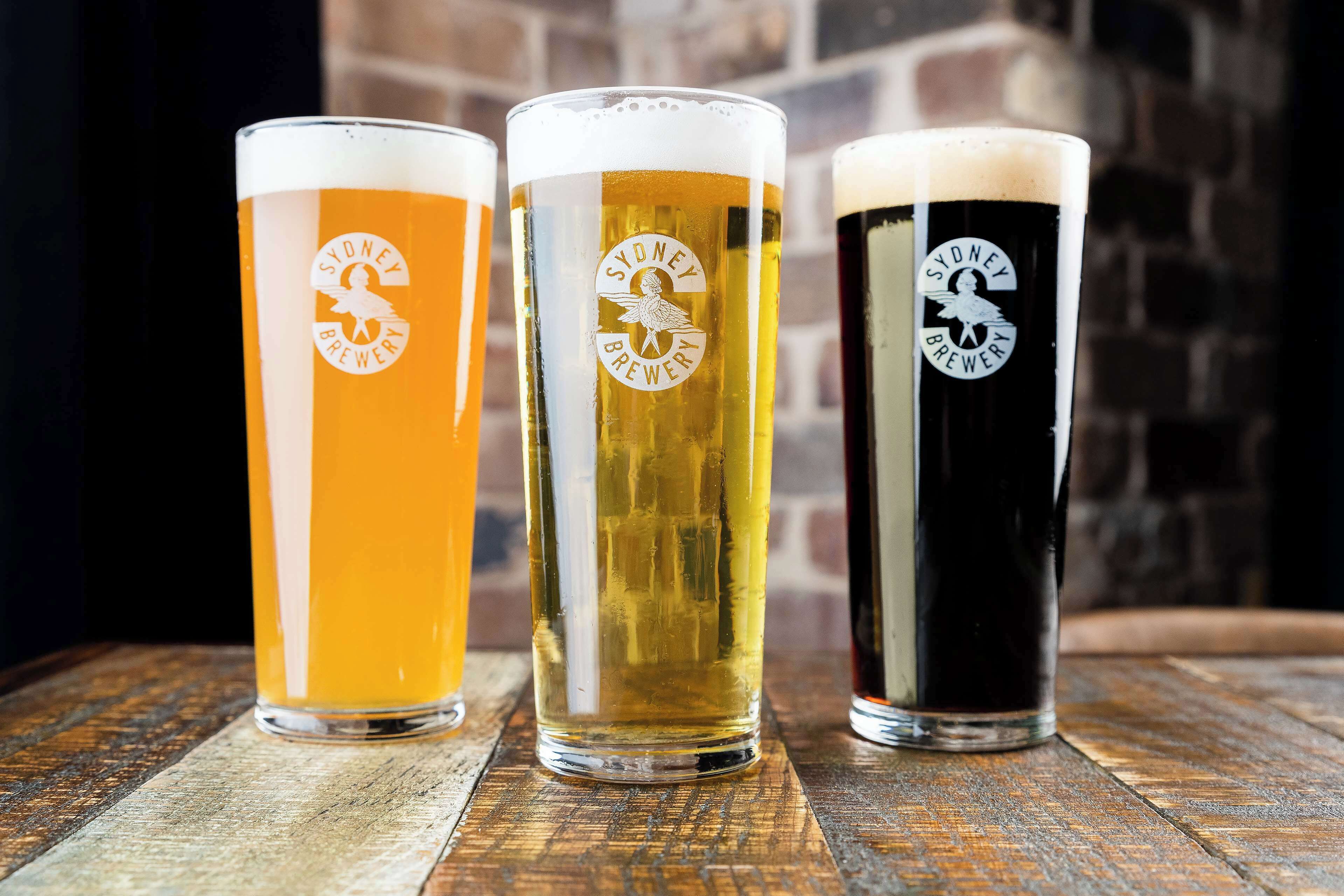 Three glasses of beer with different colors on a wooden surface.