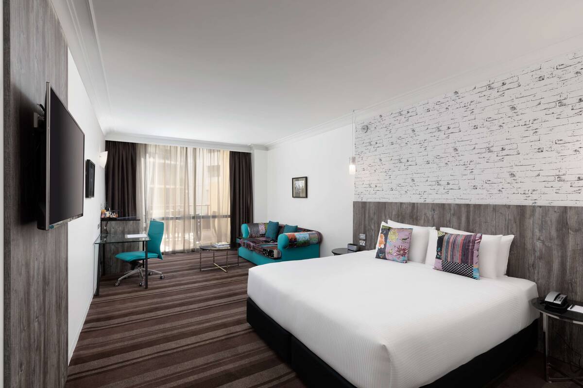 A hotel room with a large bed, a desk with a chair, a sofa, and a television.