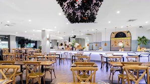Un restaurant spacieux avec des tables et des chaises en bois, un bar central et une décoration florale suspendue.