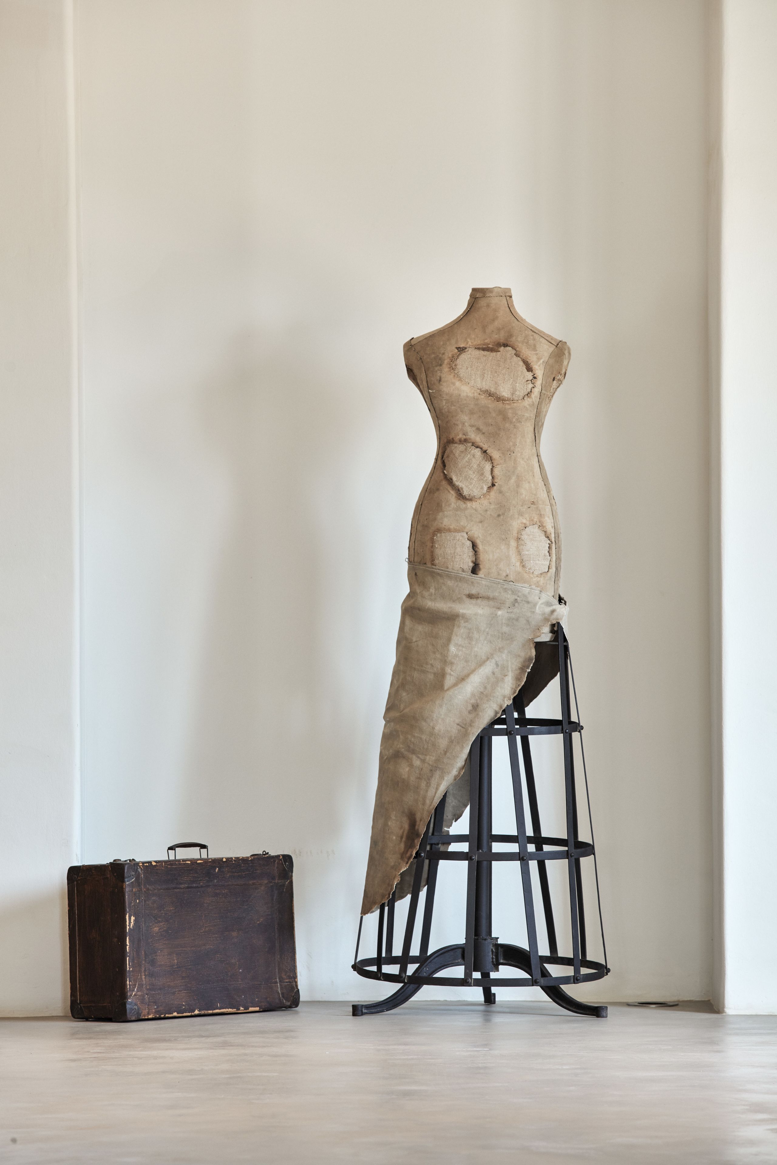 A mannequin in a dress form with a suitcase beside it.