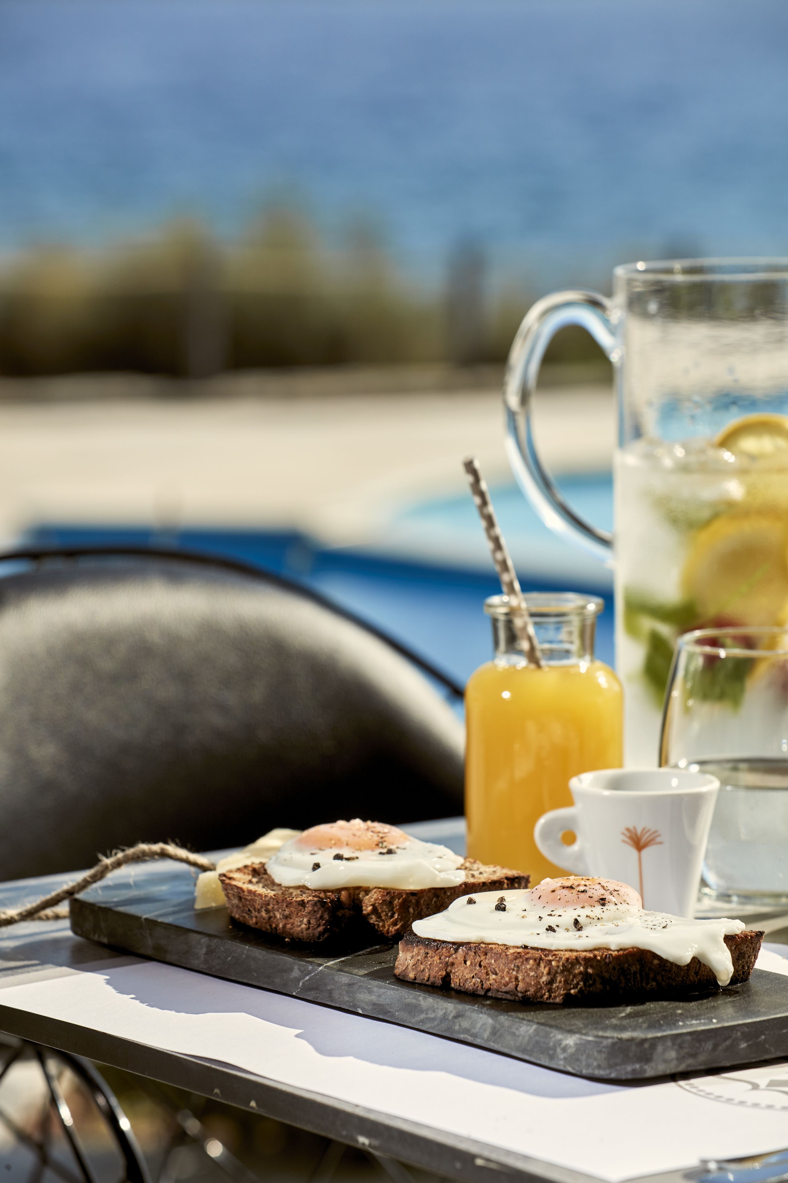 A breakfast tray with toast and eggs, a glass of orange juice, and a pitcher of iced tea with lemon slices.