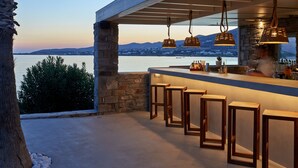 A modern outdoor bar area with stone walls, wooden bar stools, and hanging pendant lights.