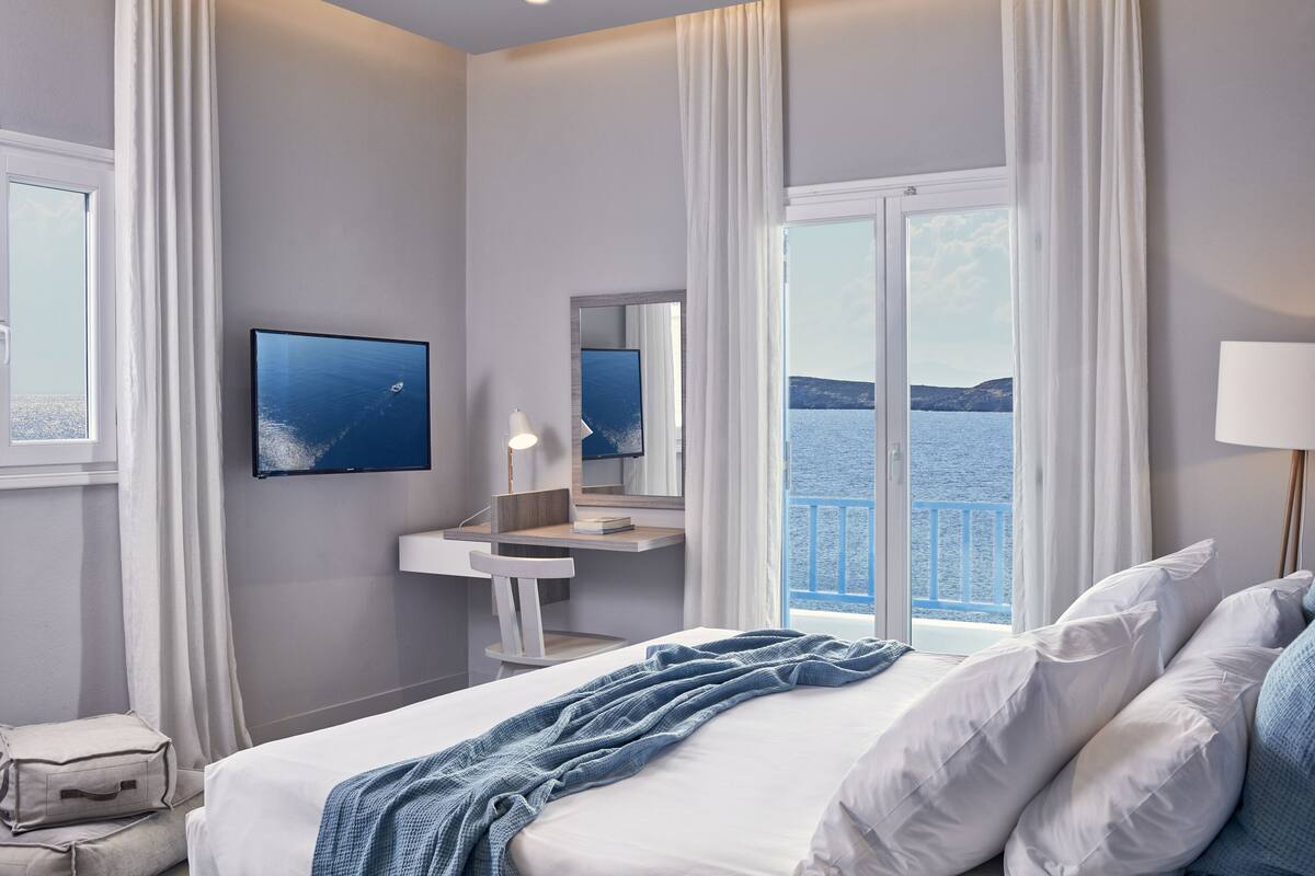 Ein Hotelzimmer mit Bett, Schreibtisch, Spiegel, Fernseher und Meerblick.