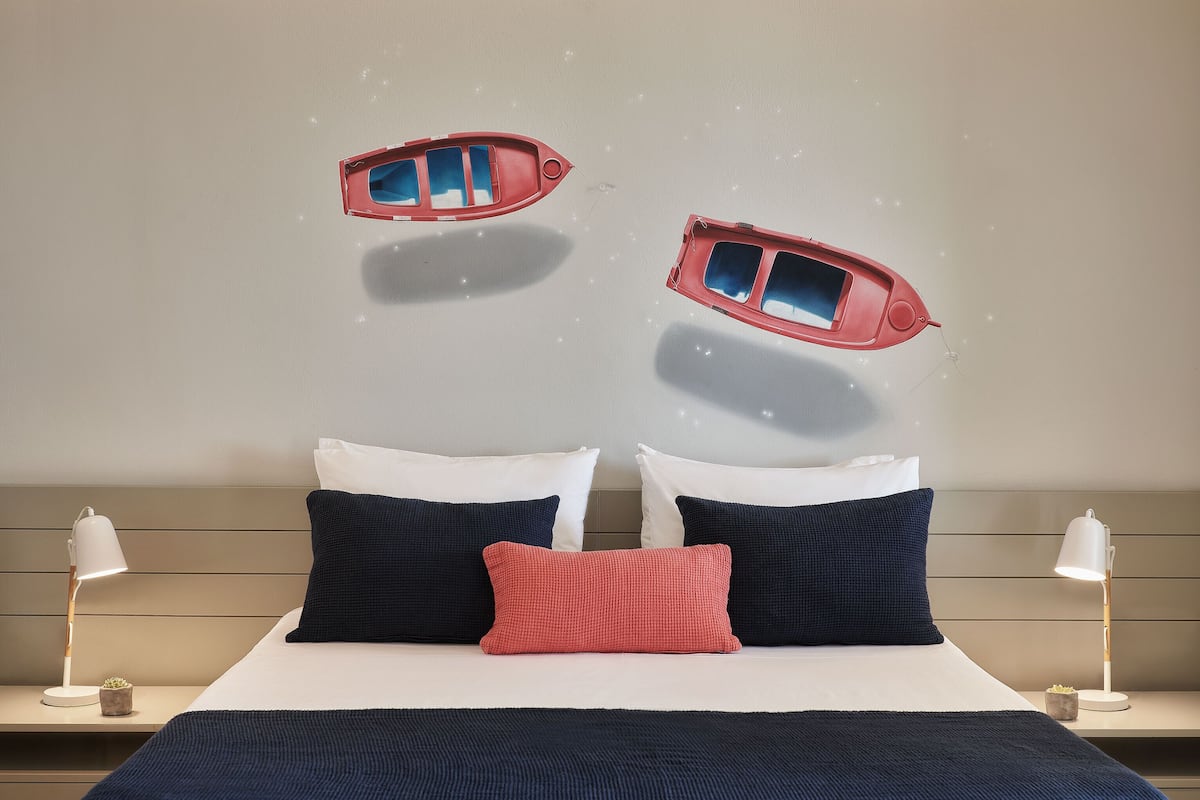 Ein Bett mit zwei Kissen, ein Nachttisch mit Lampe und eine Wand mit dekorativen Elementen.