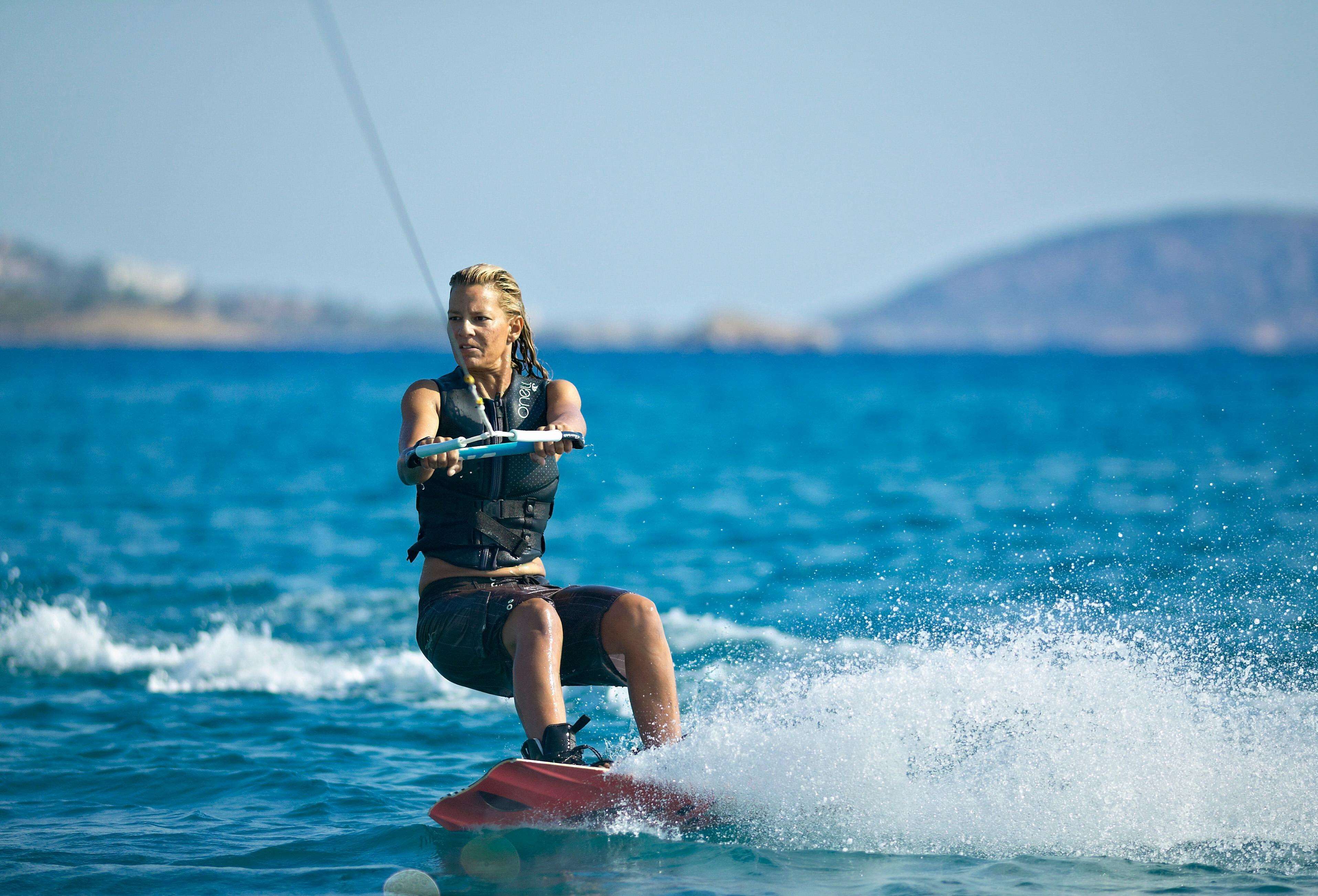 En person som åker wakeboard på ett vattendrag med en klar himmel och ett avlägset landskap i bakgrunden.