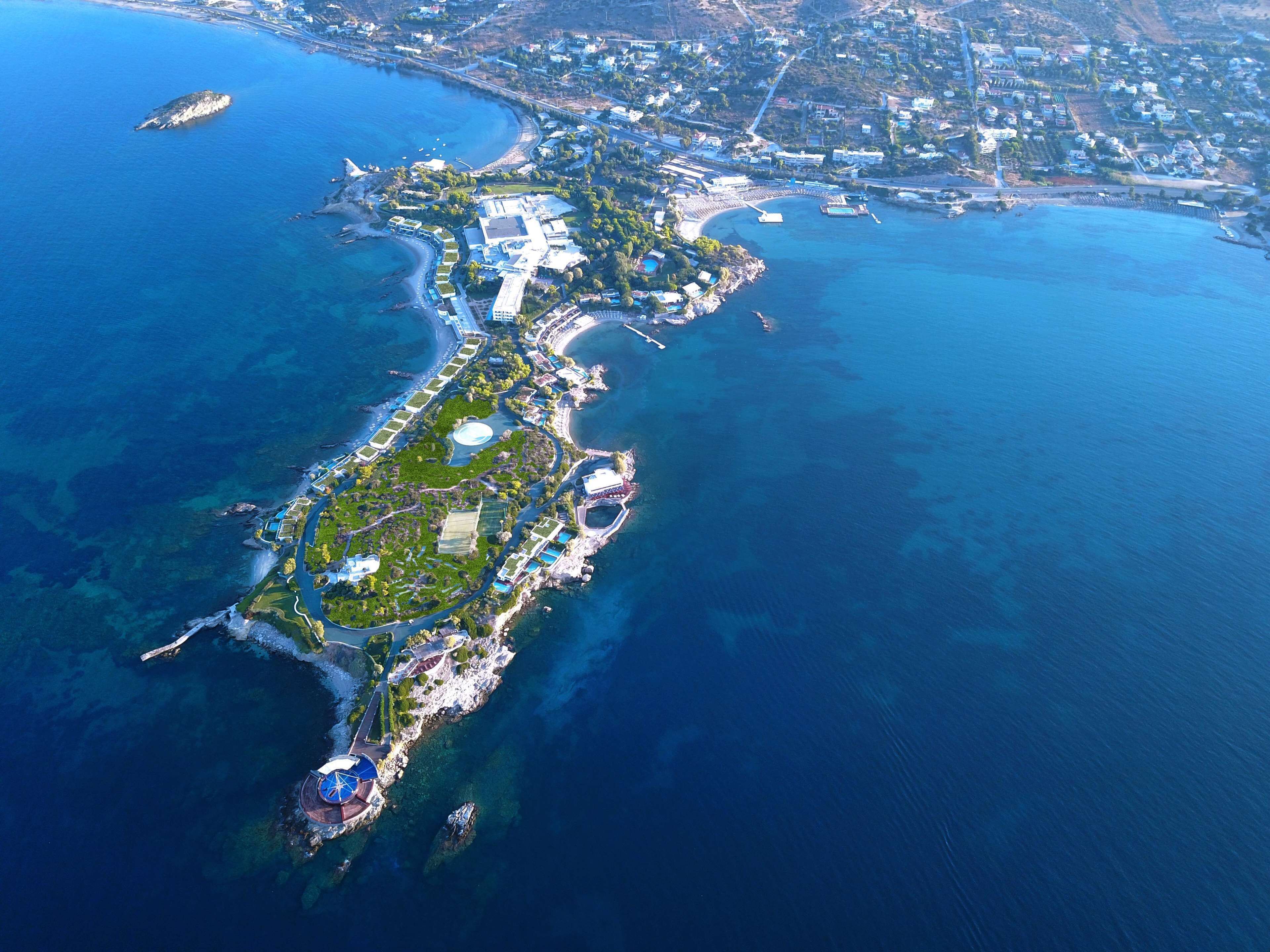 Vue aérienne d’une station balnéaire comprenant un port de plaisance, une plage et un espace paysager central avec des allées et des bâtiments.