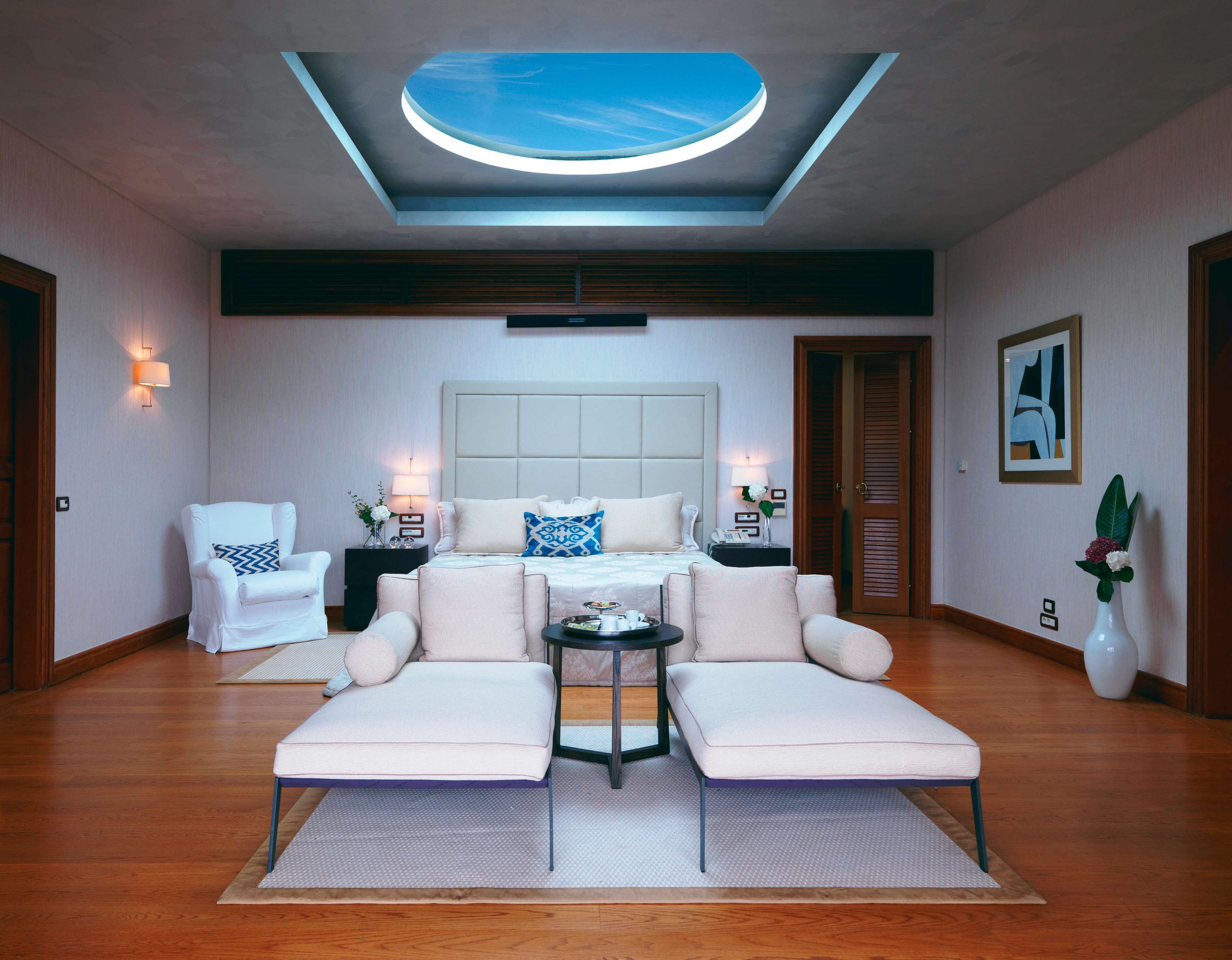 Una habitación de hotel moderna con tragaluz, una cama grande, dos sillones, una mesita auxiliar y una mesita de noche.