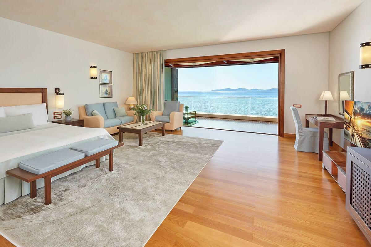 Ein Hotelzimmer mit einem Bett, zwei Sofas, einem Couchtisch, einem Schreibtisch und Blick auf das Meer.
