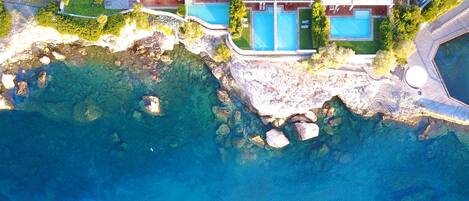 Vista aérea de una propiedad costera con varias piscinas, un litoral rocoso y abundante vegetación.