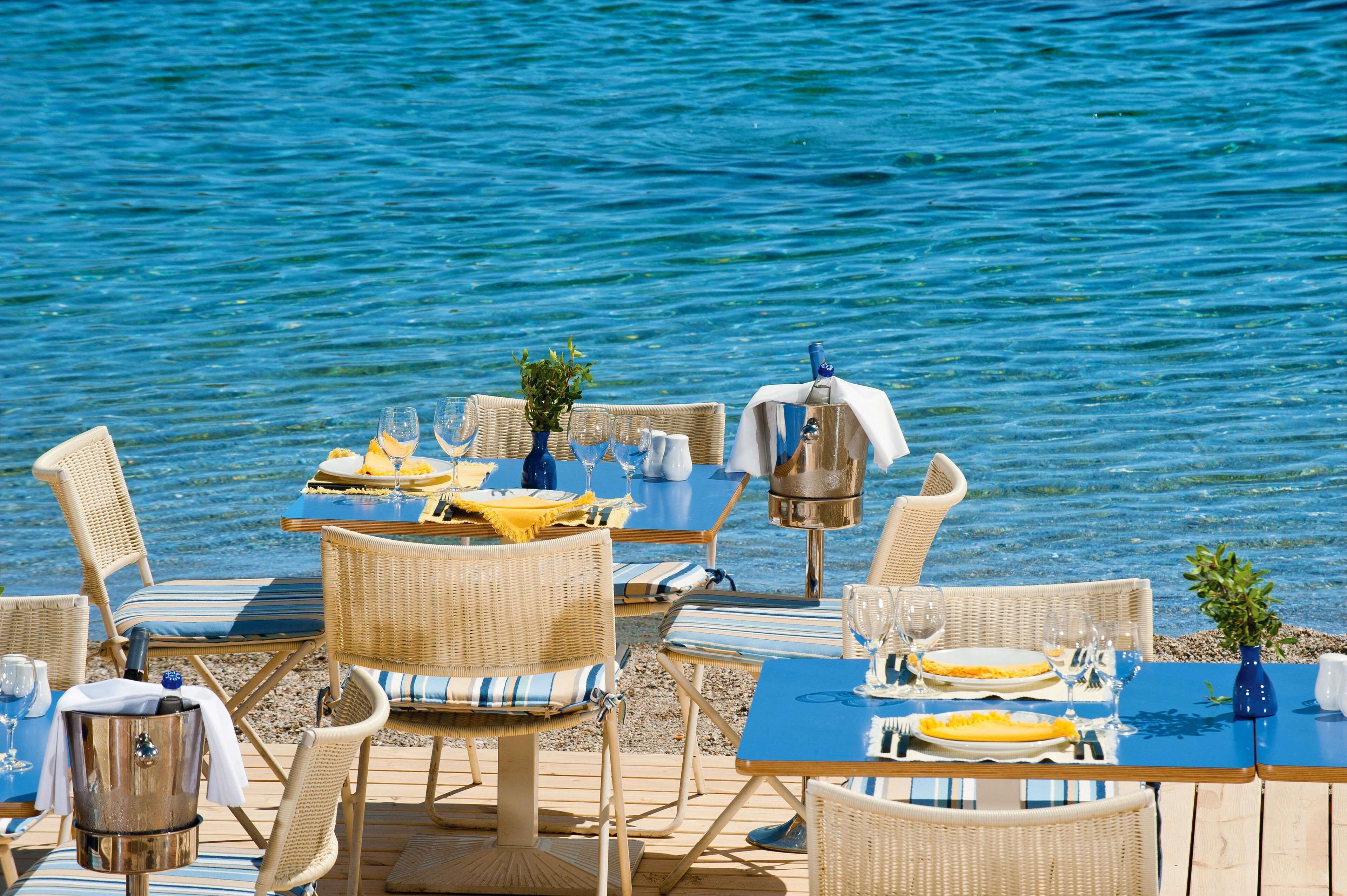 Un área de comedor frente al mar con sillas y mesas de mimbre, una parrilla y vistas al océano.