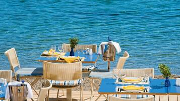 A seaside dining area with wicker chairs and tables, a grill, and a view of the sea.