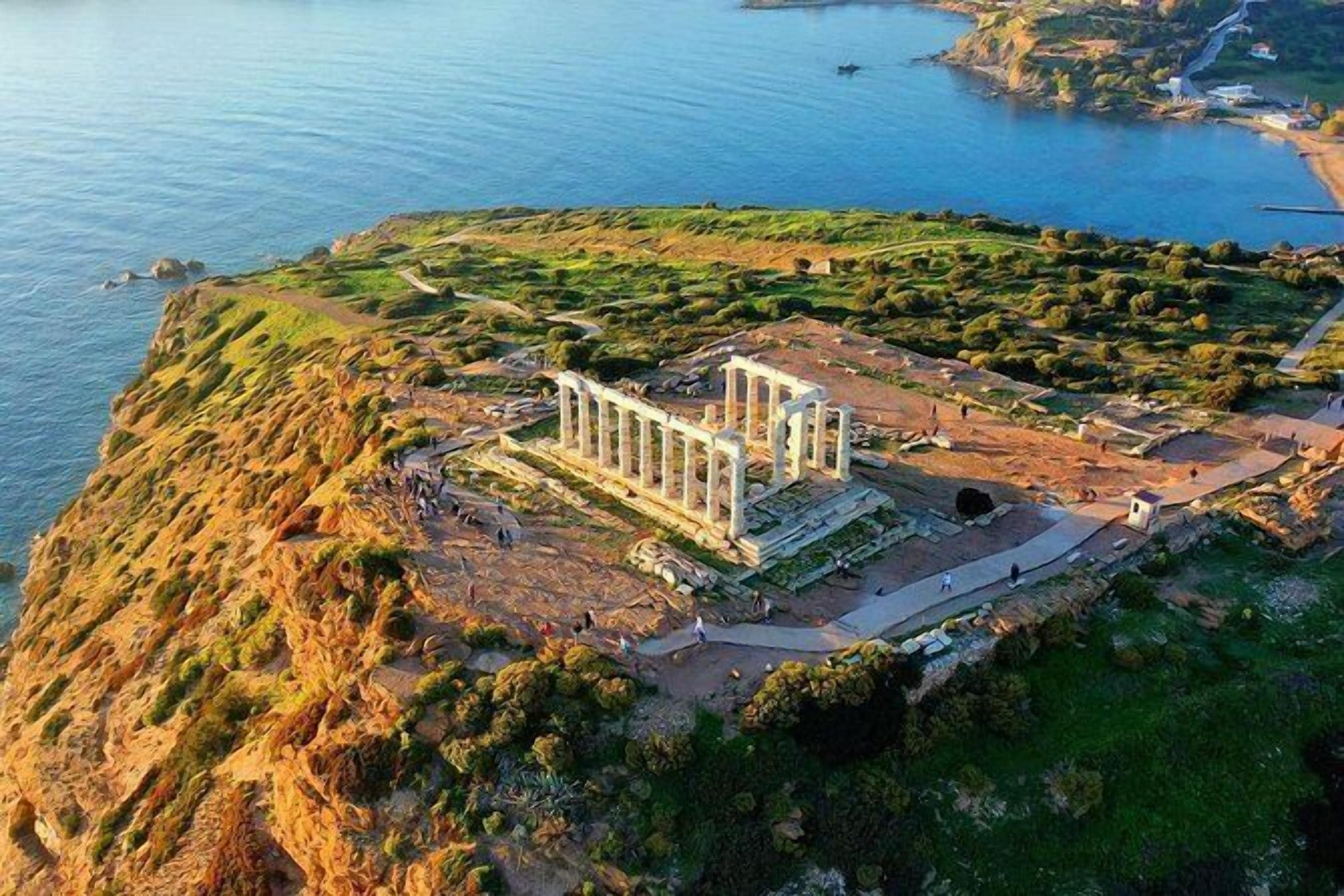 Ruinas antiguas con columnas, rodeadas de vegetación y una masa de agua.