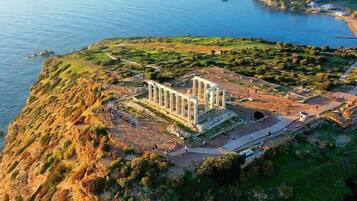 Ruinas antiguas con columnas, rodeadas de vegetación y una masa de agua.