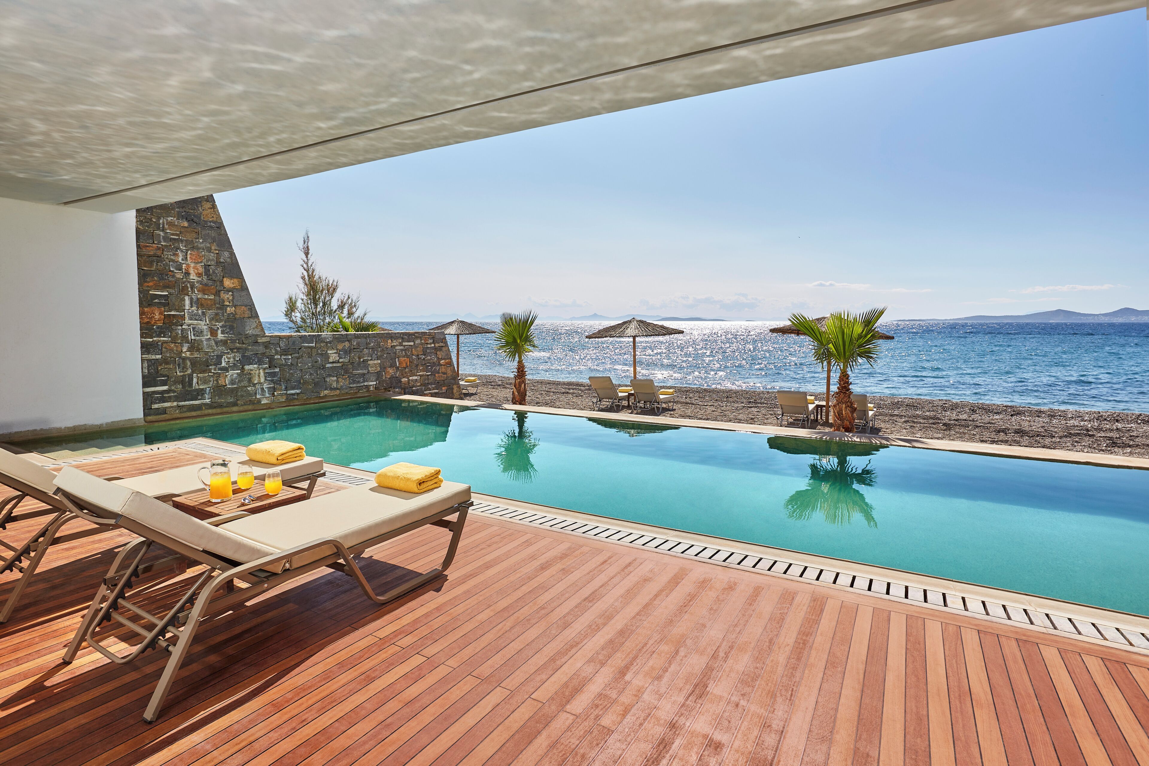 Un espace aménagé au bord de la piscine, avec des chaises longues, un mur en pierre et une vue sur la mer.