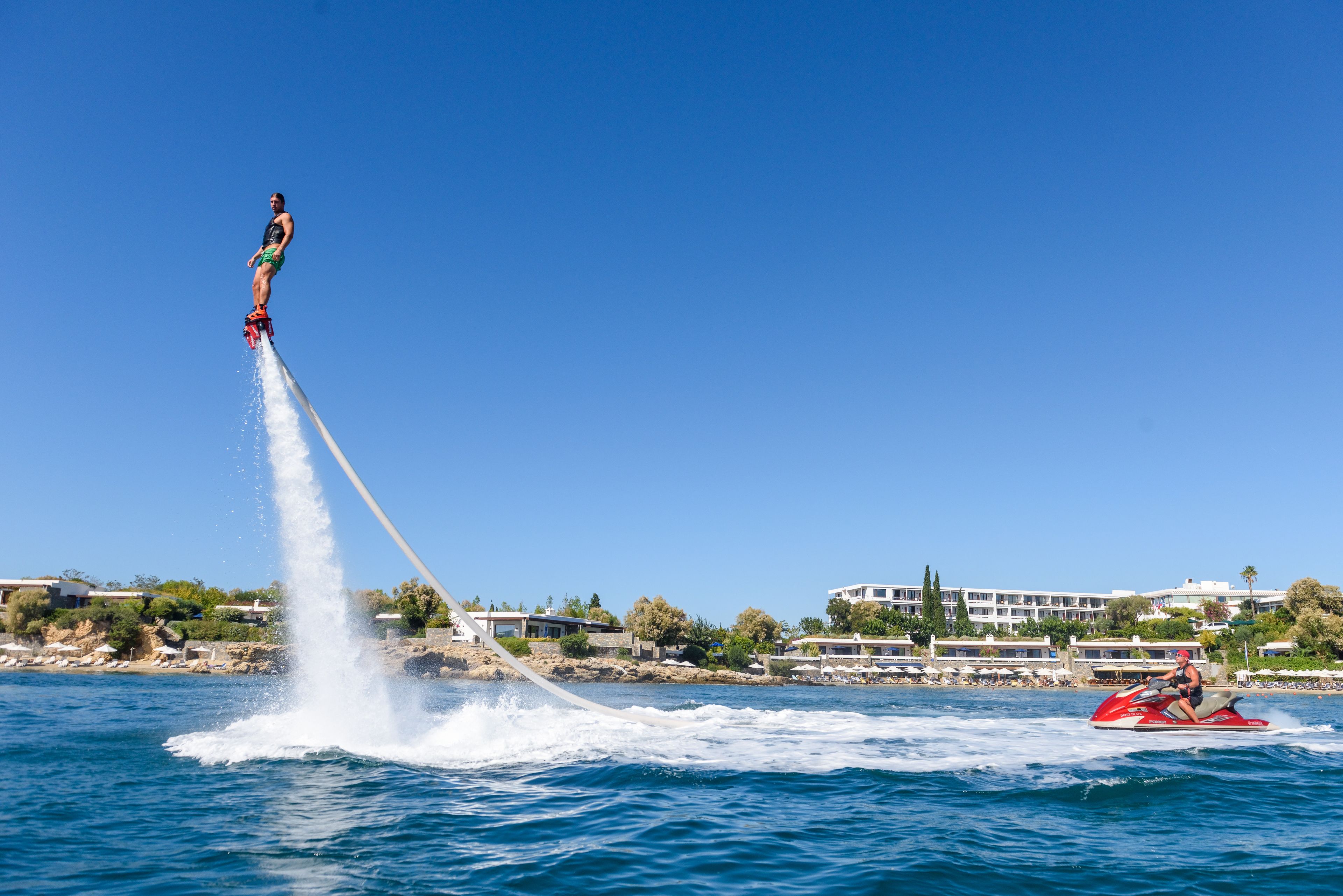 A person jet-skiing with a tow rope, a red jet ski, and a building in the background.