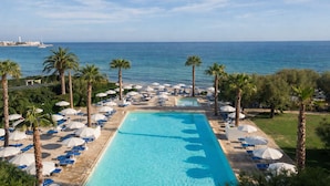 A pool area with clear blue water, surrounded by palm trees and lounge chairs, overlooking a calm sea. - Hotel Del Levante (Fasano)