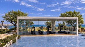 A modern outdoor gym with exercise equipment, surrounded by glass walls offering a view of the sea and cityscape. - Hotel Del Levante (Fasano)