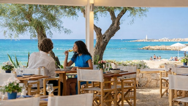 An outdoor dining area with tables and chairs, overlooking a beach and the sea. - Hotel Del Levante (Fasano)