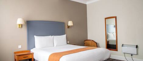 A hotel room with a large bed, a bedside table, a chair, a mirror, and a radiator.