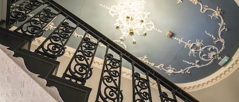 Een trap met sierlijke zwarte leuningen en een plafond met decoratieve witte patronen, inclusief een centrale kroonluchter.
