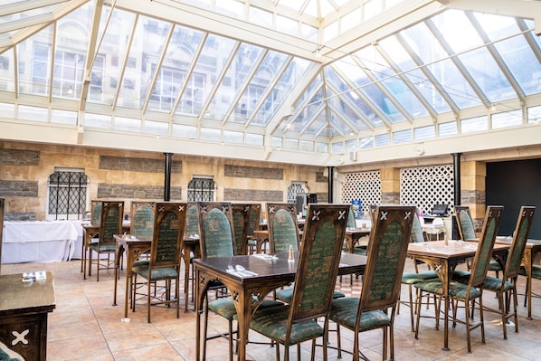 A restaurant with a glass ceiling, wooden tables, and green upholstered chairs. - Arnos Manor Hotel (Bristol)