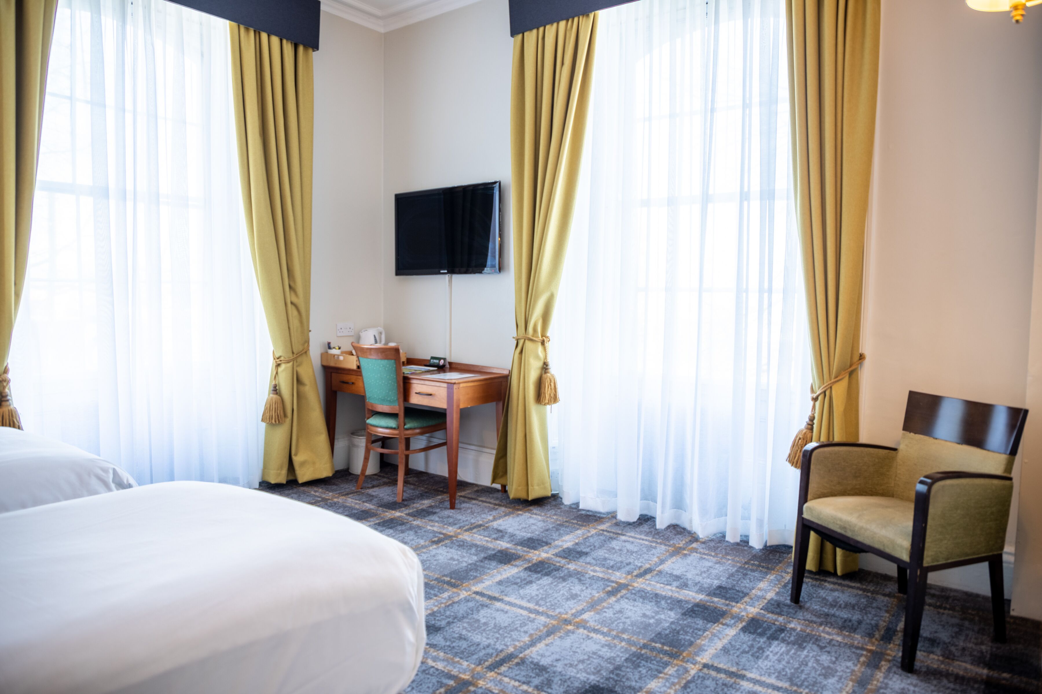 A hotel room with a bed, a desk, a chair, a television, and curtains.