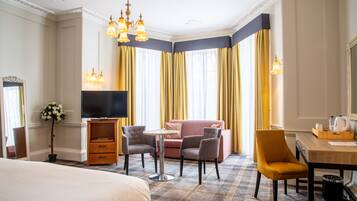 A hotel room with a bed, a TV, a sofa, two chairs, a small table, and a desk with a chair.