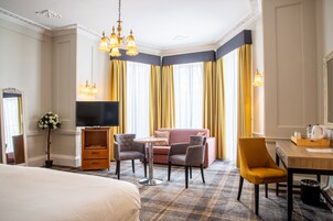 Une chambre d’hôtel comprenant un lit, une télévision, un canapé, deux fauteuils, une petite table et un bureau avec une chaise.