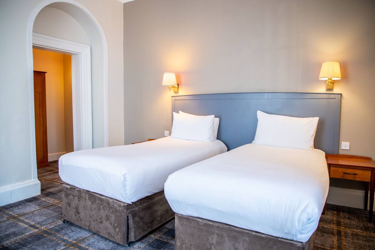 Una habitación de hotel con dos camas, una mesita de noche de madera y dos lámparas de pared.