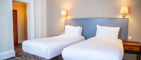 Ein Hotelzimmer mit zwei Betten, einem Nachttisch aus Holz und zwei Wandleuchten.