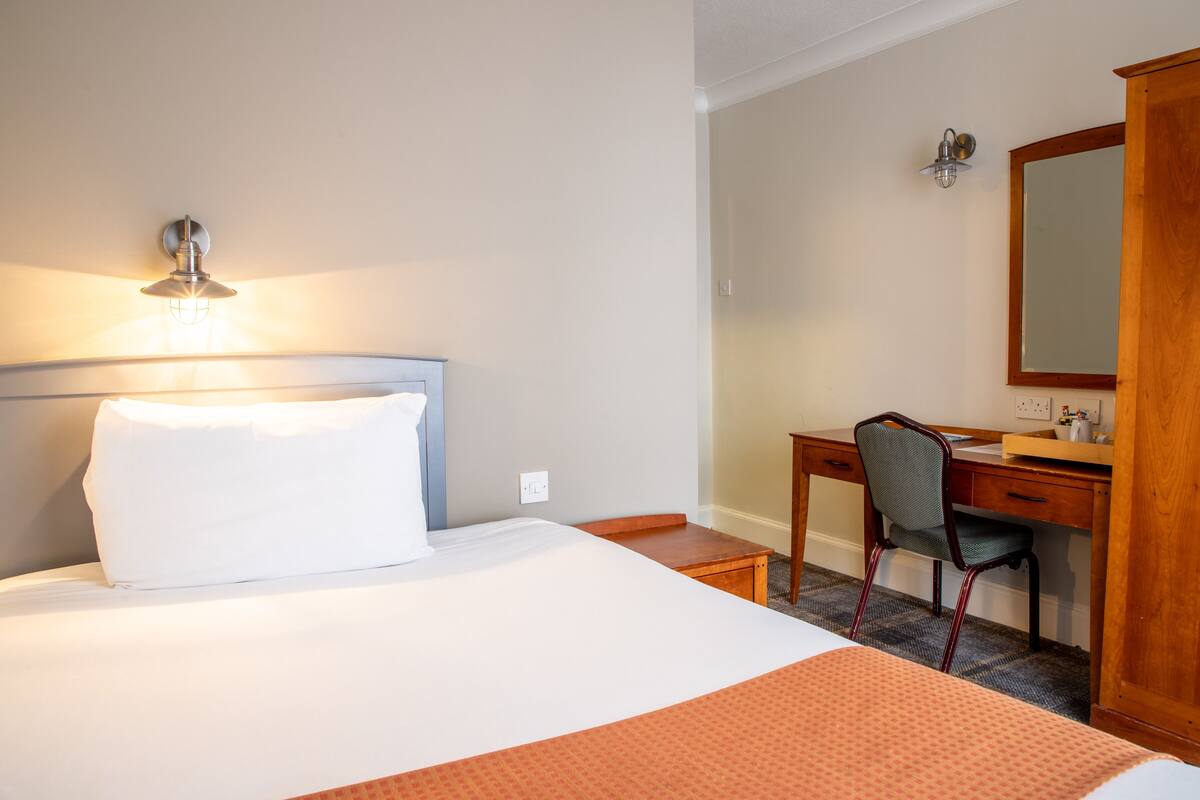 Una habitación de hotel con cama, escritorio, silla y espejo.