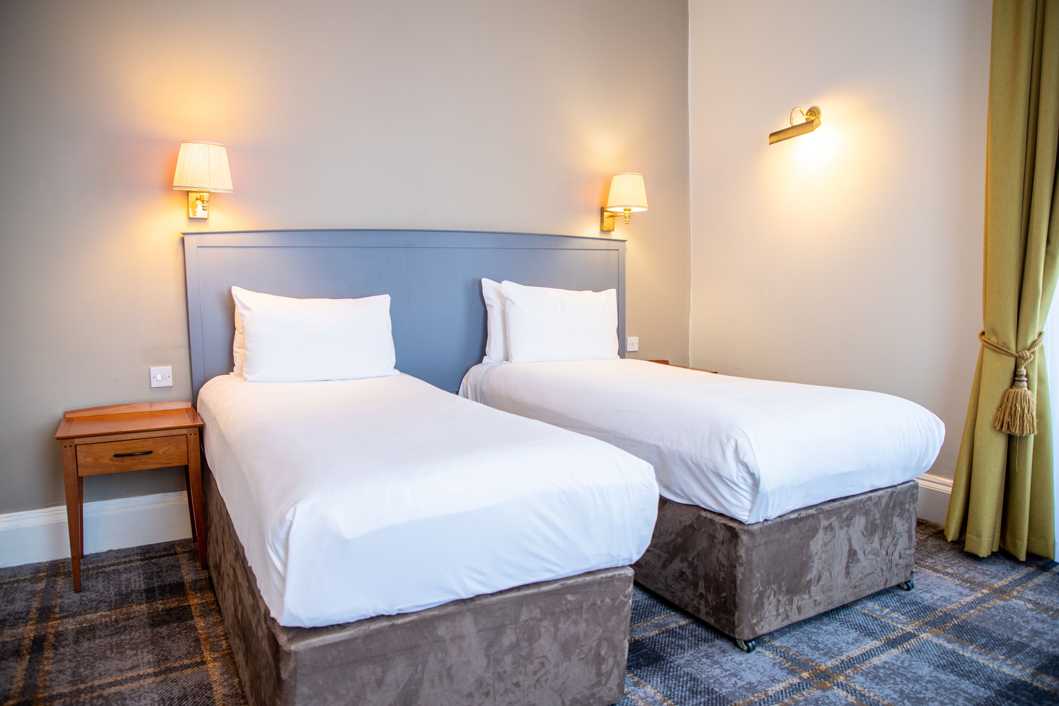 Une chambre d’hôtel avec deux lits, chacun doté de draps blancs et d’une tête de lit bleue. Deux lampes murales sont fixées de part et d’autre des lits.