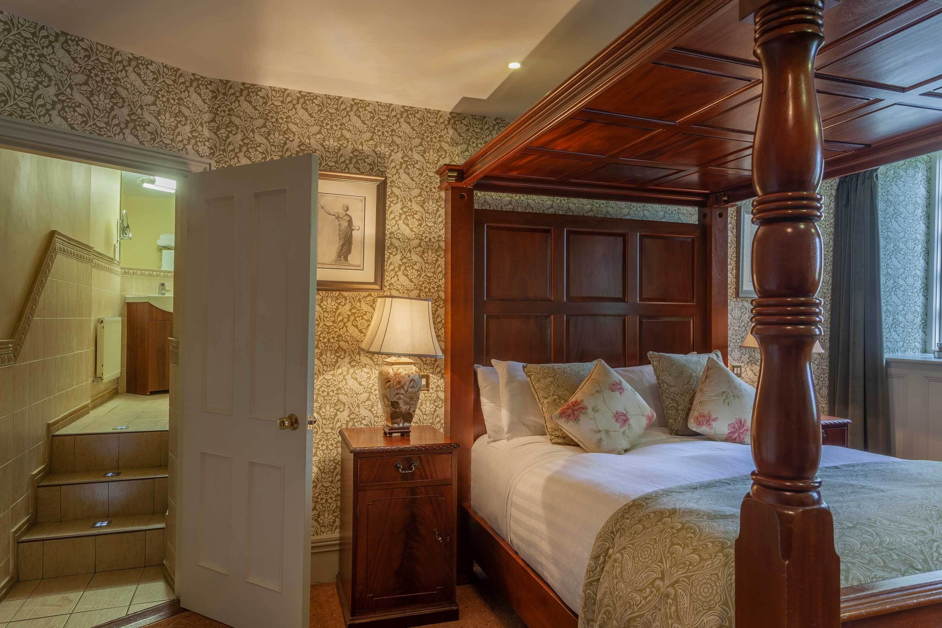 A four-poster bed with a wooden headboard, a nightstand with a lamp, and a framed picture on the wall.