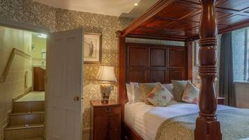 A four-poster bed with a wooden headboard, a nightstand with a lamp, and a framed picture on the wall.