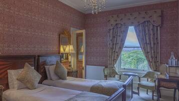 Quarto de hotel com duas camas, área de estar com mesa e cadeiras, um lustre e vista pela janela.