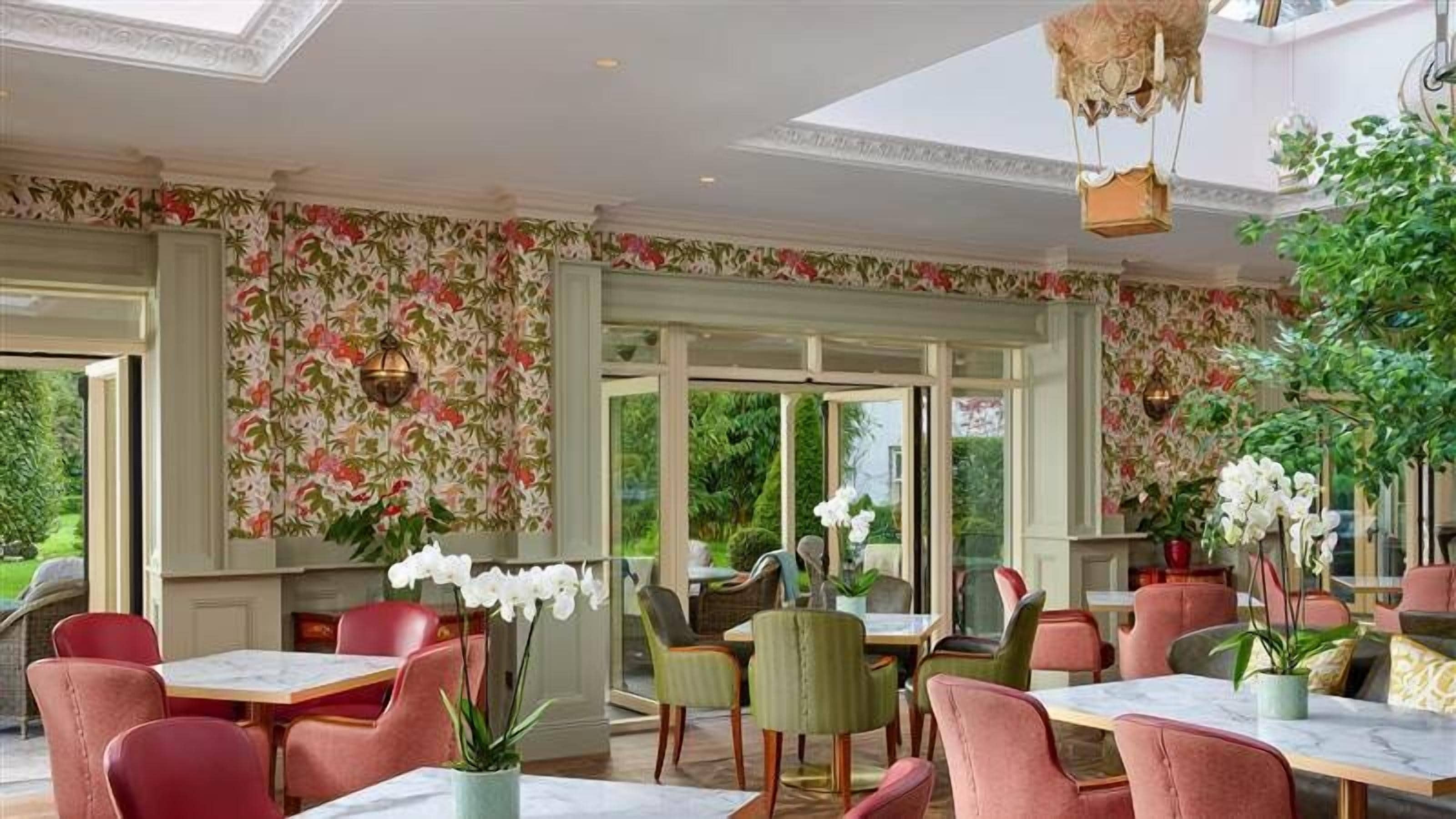 Un restaurant avec un papier peint à motifs floraux, des chaises vertes et rouges, et un luminaire suspendu.