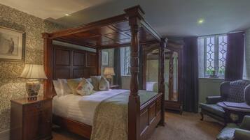 A four-poster bed with a wooden frame, a nightstand with a lamp, a chair, and a window with curtains.