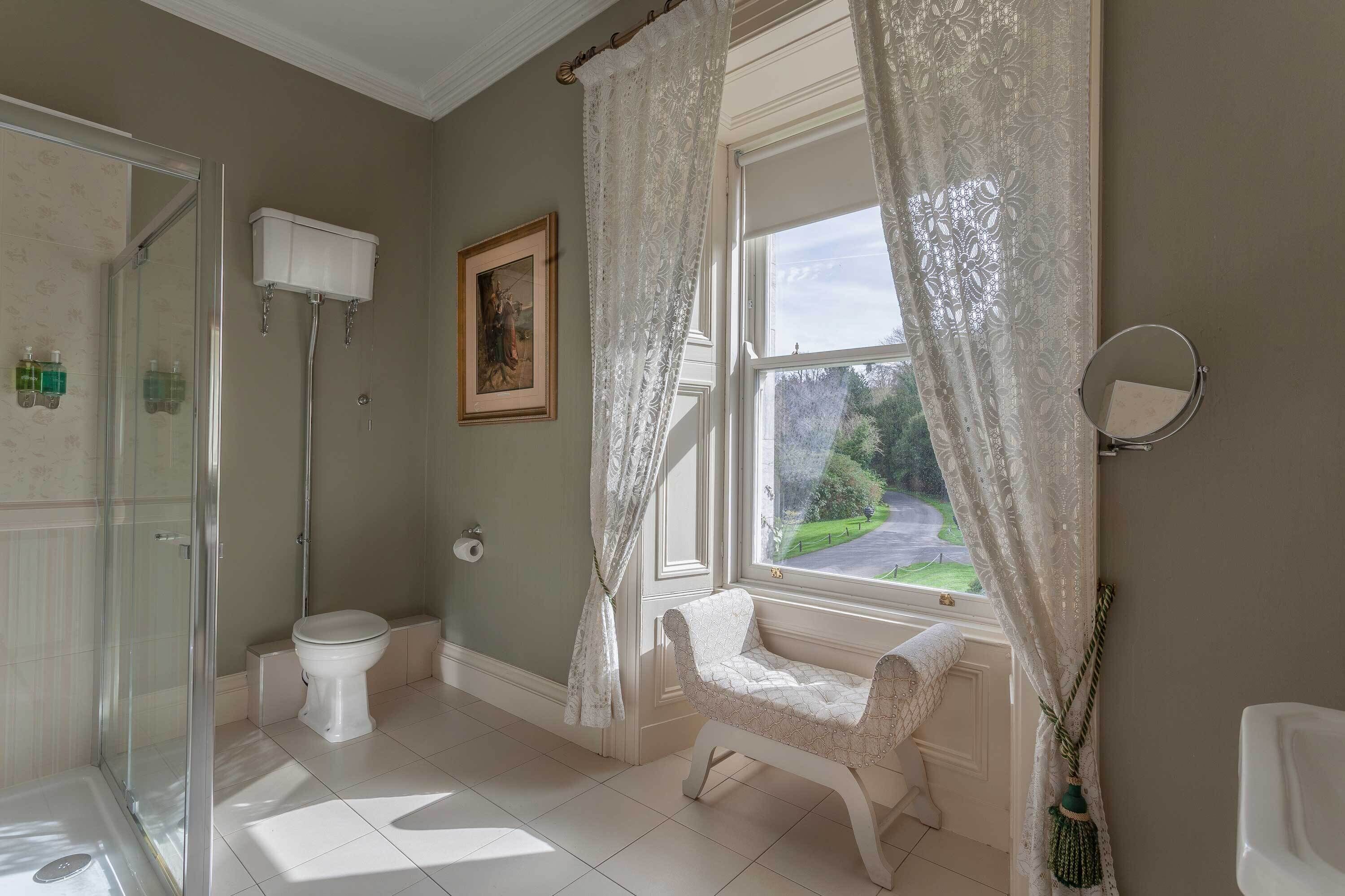 A bathroom with a toilet, shower, and window with curtains.