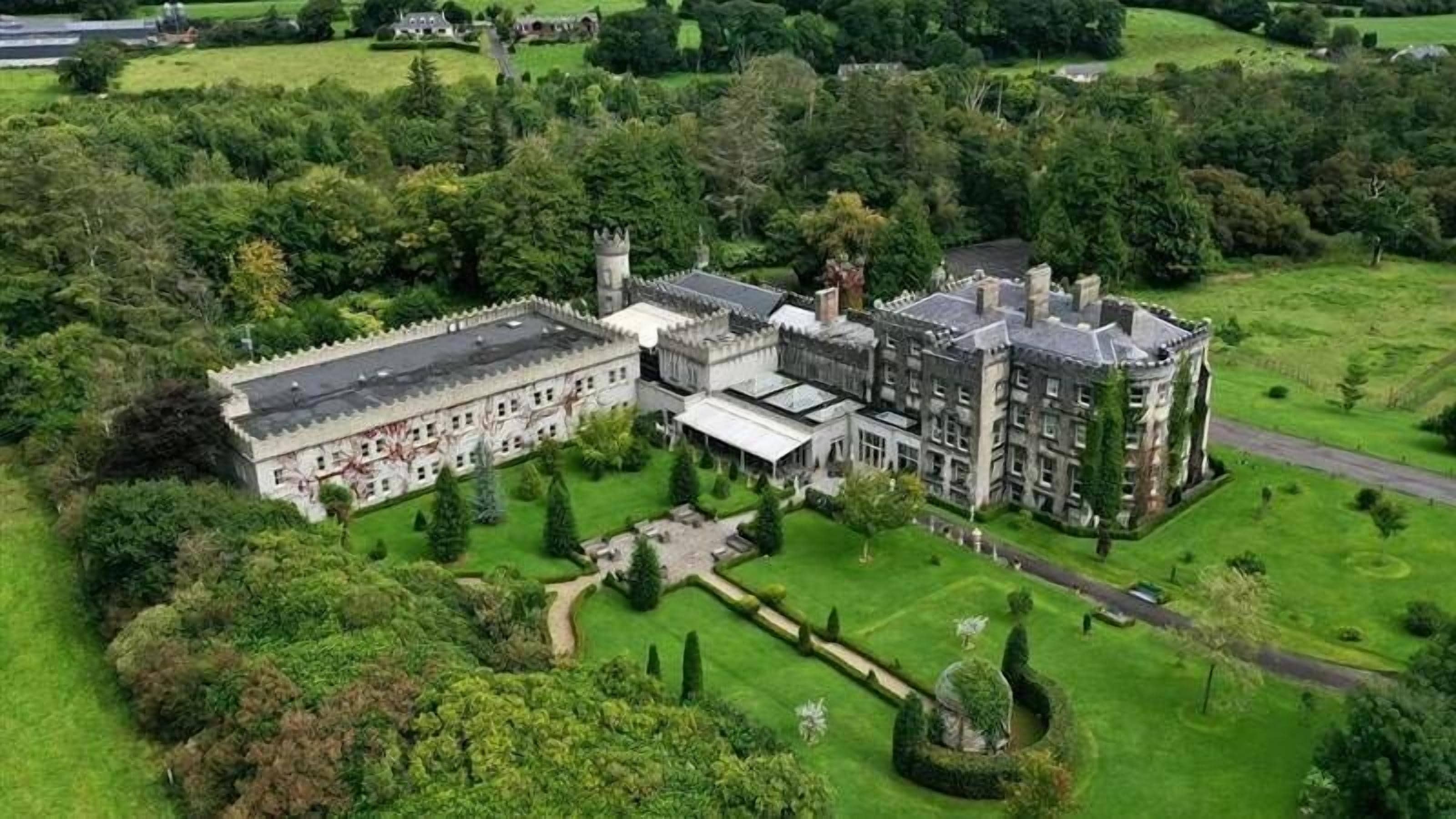 A large, historic building with multiple wings, surrounded by well-maintained gardens and a moat.