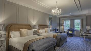 A hotel room with two beds, a chandelier, a desk, and a view of the outdoors.