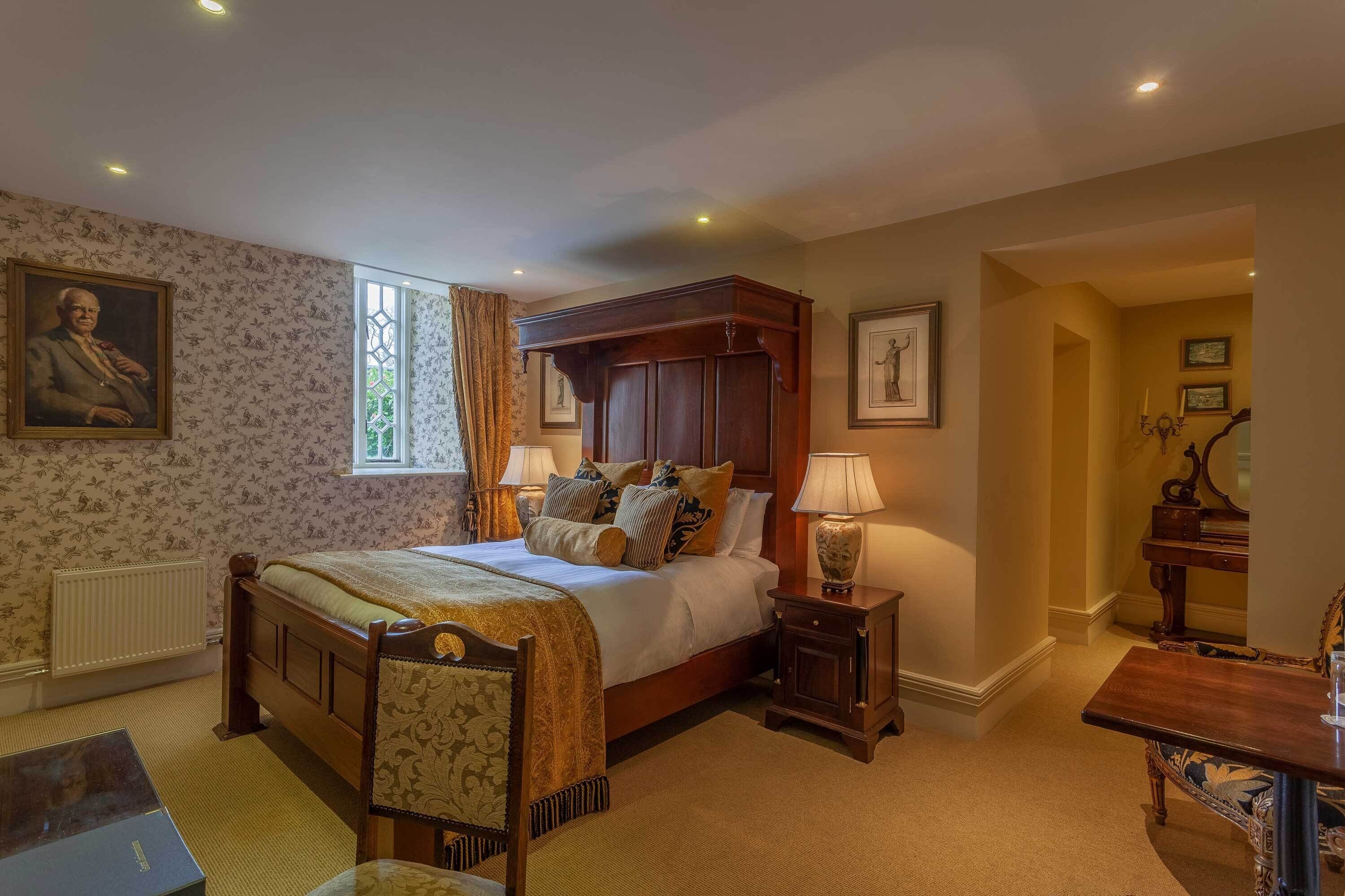 A bedroom with a large bed, a bedside table with a lamp, a chair, a desk, and a radiator.