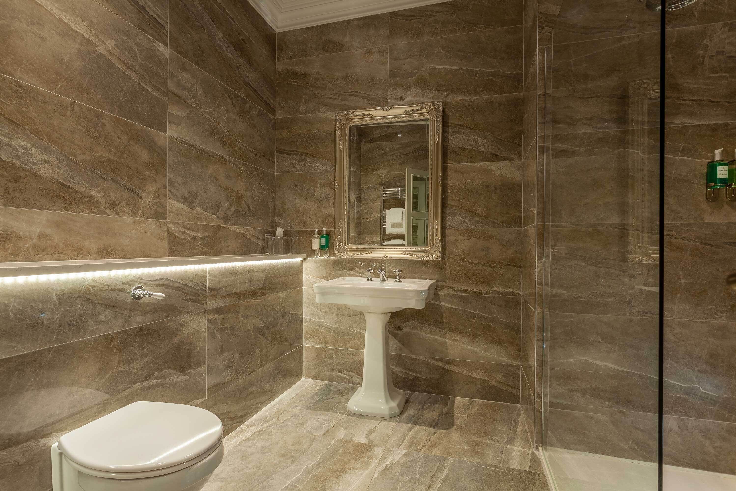 A bathroom with a pedestal sink, a toilet, and a large mirror.