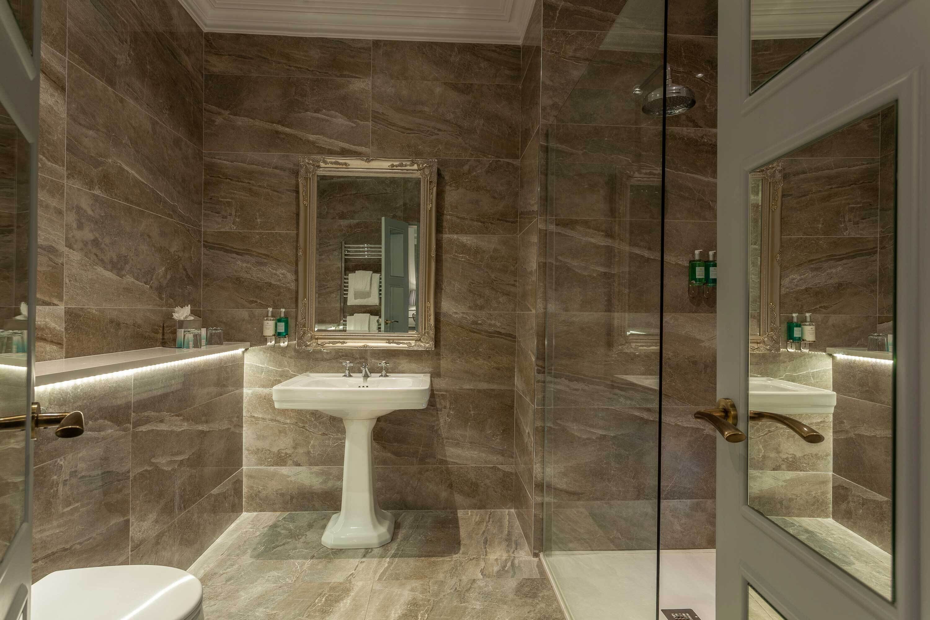 Un baño con lavamanos pedestal, un espejo grande y cabina de ducha con mampara de vidrio.