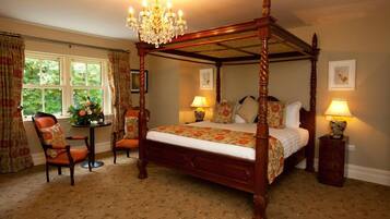 A four-poster bed with a chandelier, two bedside tables with lamps, a chair, and a window with curtains.