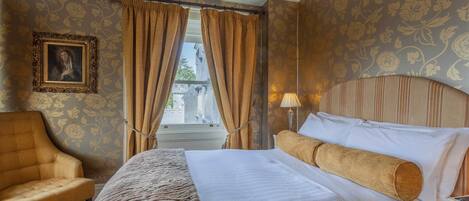 A hotel room with a bed, a chair, a lamp, and a window with curtains.